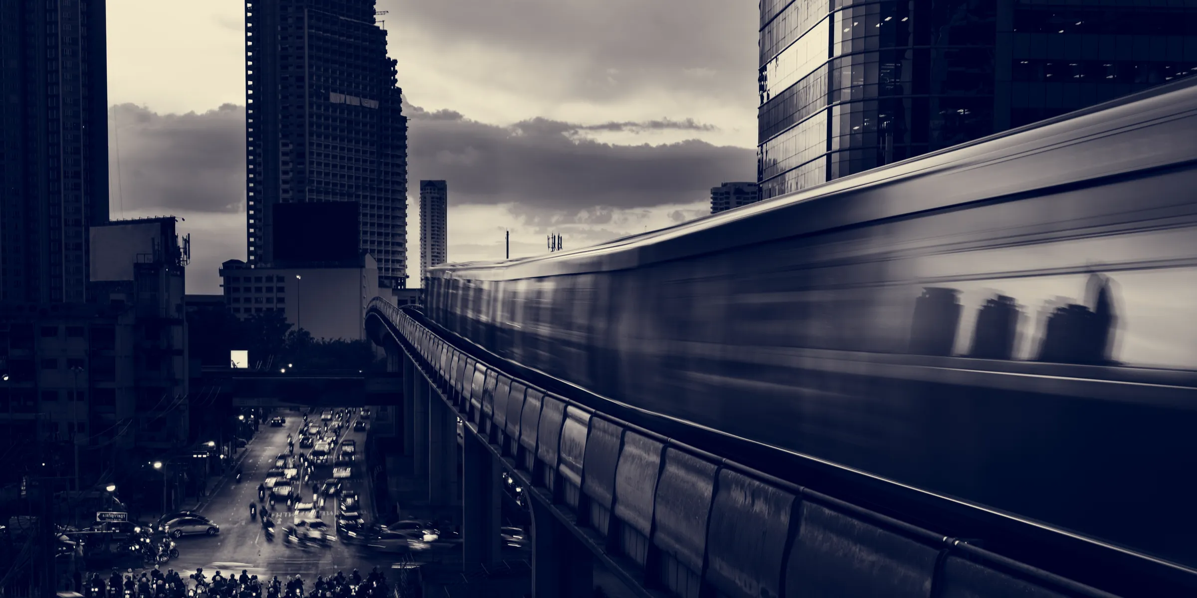 Trem elevado em movimento entre edifícios de uma grande cidade, em preto e branco